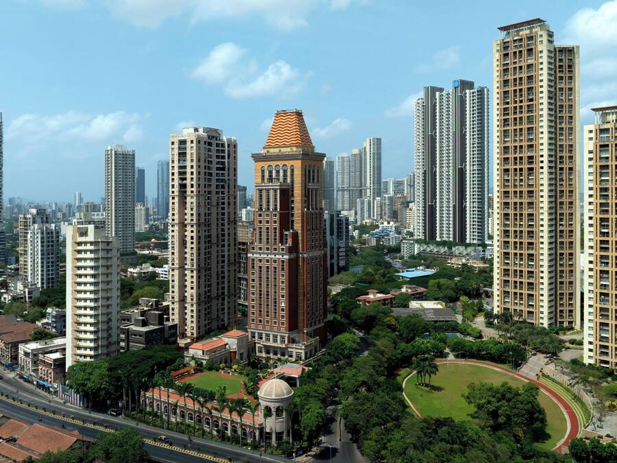 Un edificio de gran altura con una torre distintiva, rodeado de otros edificios residenciales altos, una carretera y zonas verdes.
