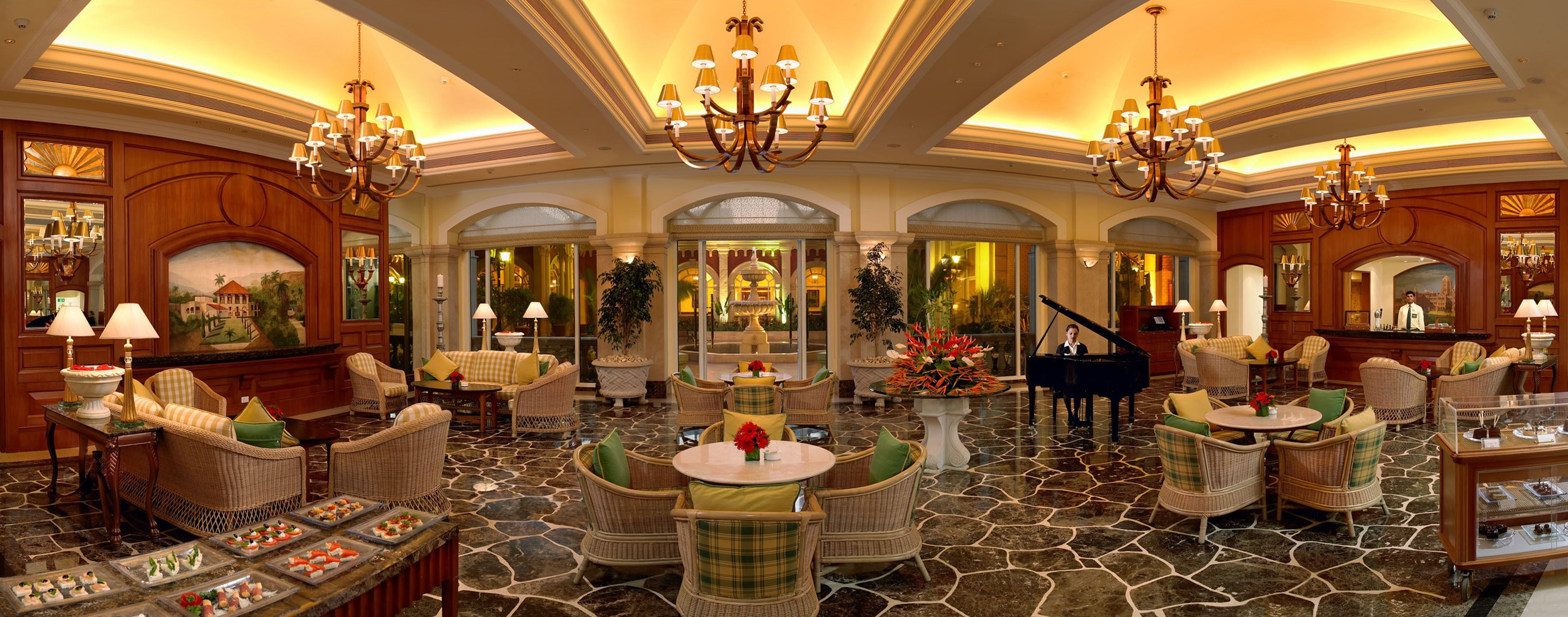 A luxurious lobby with chandeliers, wicker furniture, a grand piano, and a fountain.