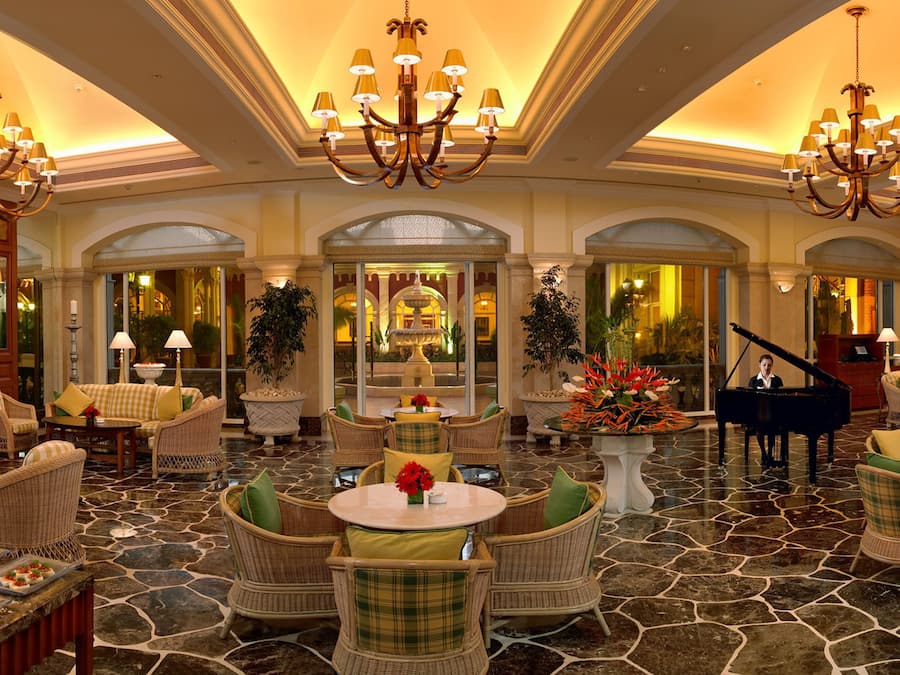 A luxurious lobby with chandeliers, wicker furniture, a grand piano, and a fountain.