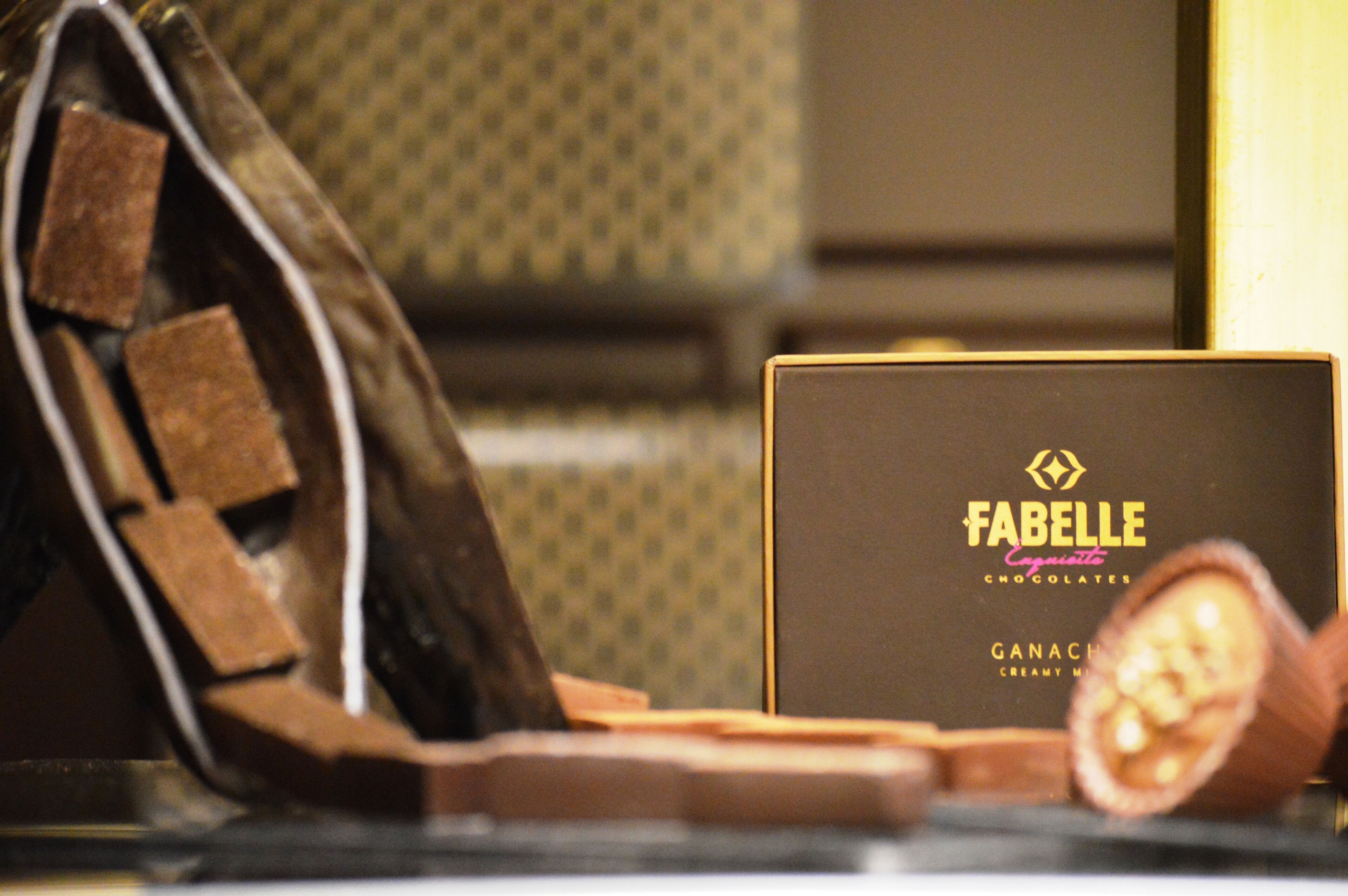 A Fablele chocolates box, a wooden spoon with chocolate, and a chocolate bar.