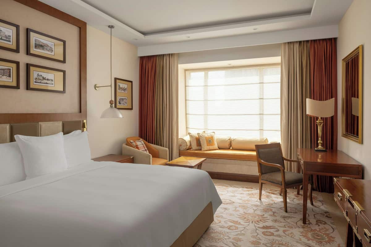 A hotel room with a large bed, a desk, a chair, a sofa, and a window with curtains.