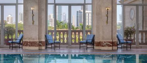 A swimming pool with lounge chairs and large windows offering city views.
