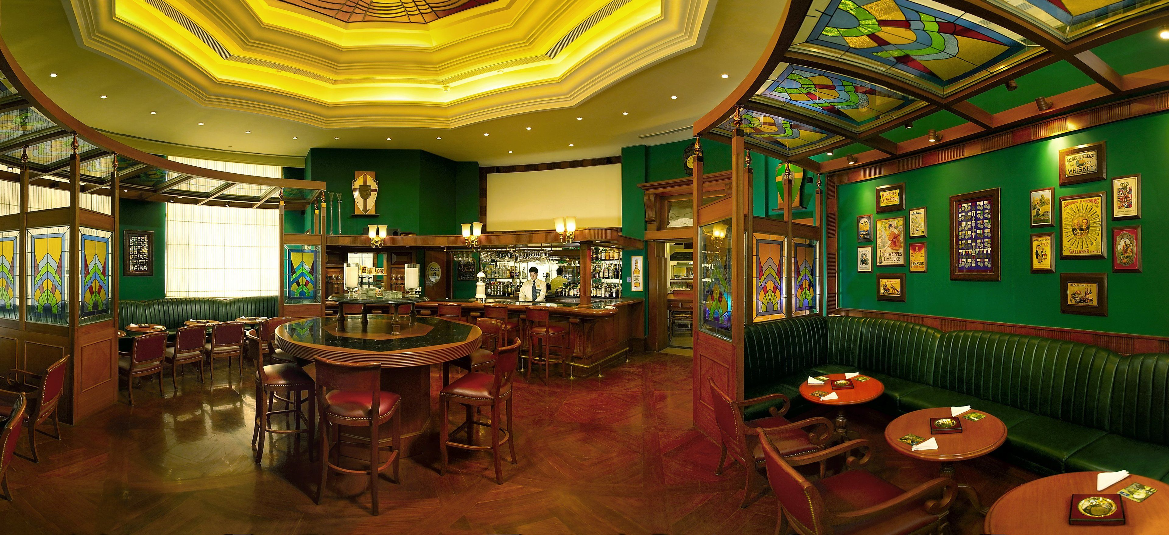 A bar area with a round bar, seating, and a green wall with framed pictures.