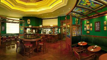 A bar area with a round bar, seating, and a green wall with framed pictures.