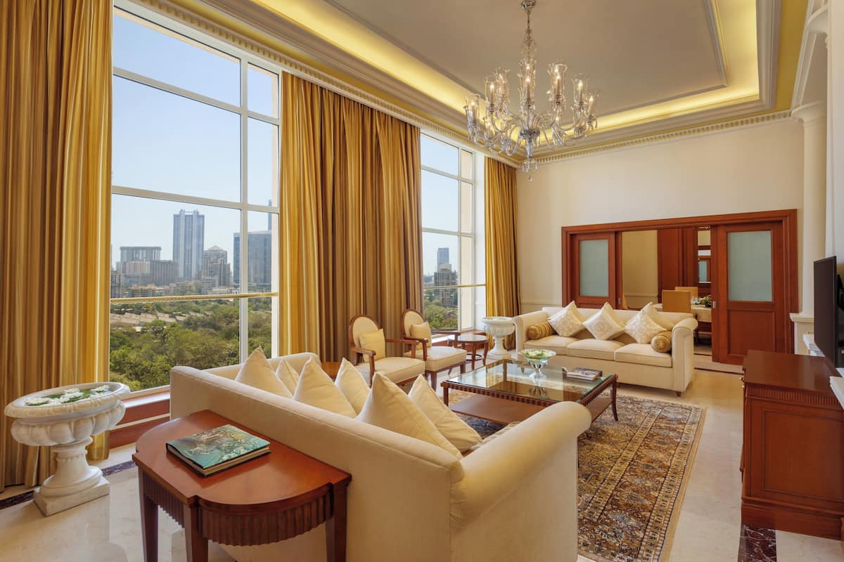 A spacious living room with a large window, a chandelier, and a view of a cityscape.