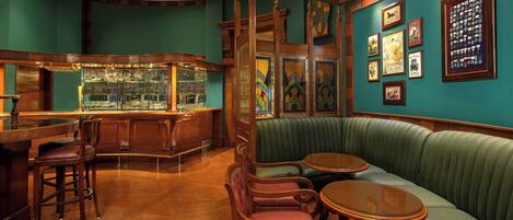 A bar area with wooden bar stools, a green upholstered booth, and framed pictures on the walls.