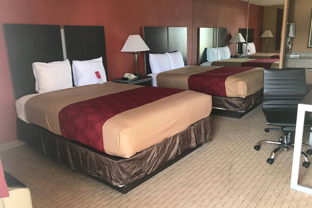 A hotel room with two beds, each with a headboard, bedside tables, lamps, and a desk with a chair.