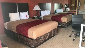 A hotel room with two beds, each with a headboard, bedside tables, lamps, and a desk with a chair.