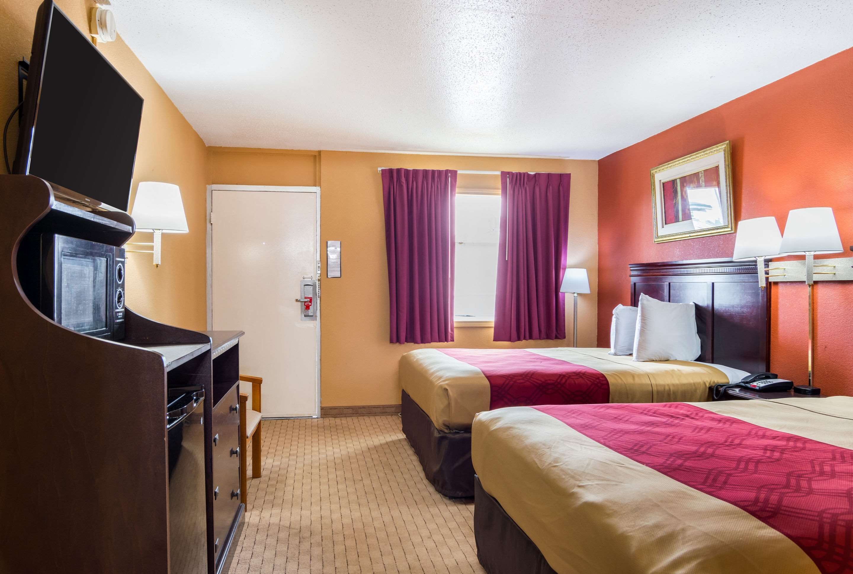 A hotel room with two beds, a desk with a TV, and a door.