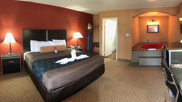 A hotel room with a bed, two bedside lamps, a desk with a chair, a red chair, and a bathroom visible through an open door. - Econo Lodge Jacksonville near Little Rock Air Force Base (Jacksonville)