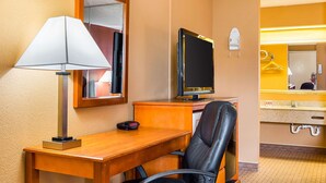 A hotel room with a wooden desk, a black leather chair, a lamp, a flat-screen TV, a mirror, and a bathroom with a sink and towel rack. - Econo Lodge Jacksonville near Little Rock Air Force Base (Jacksonville)