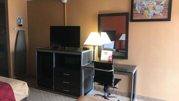 A hotel room with a bed, a desk, a television, a lamp, and a wall-mounted clock.