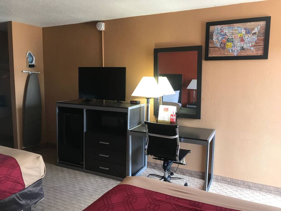 A hotel room with a bed, a desk, a television, a lamp, and a wall-mounted clock.