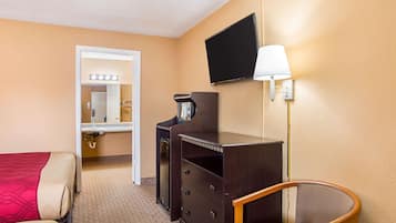 Una habitación de hotel con cama, escritorio con lámpara, televisión y una silla.