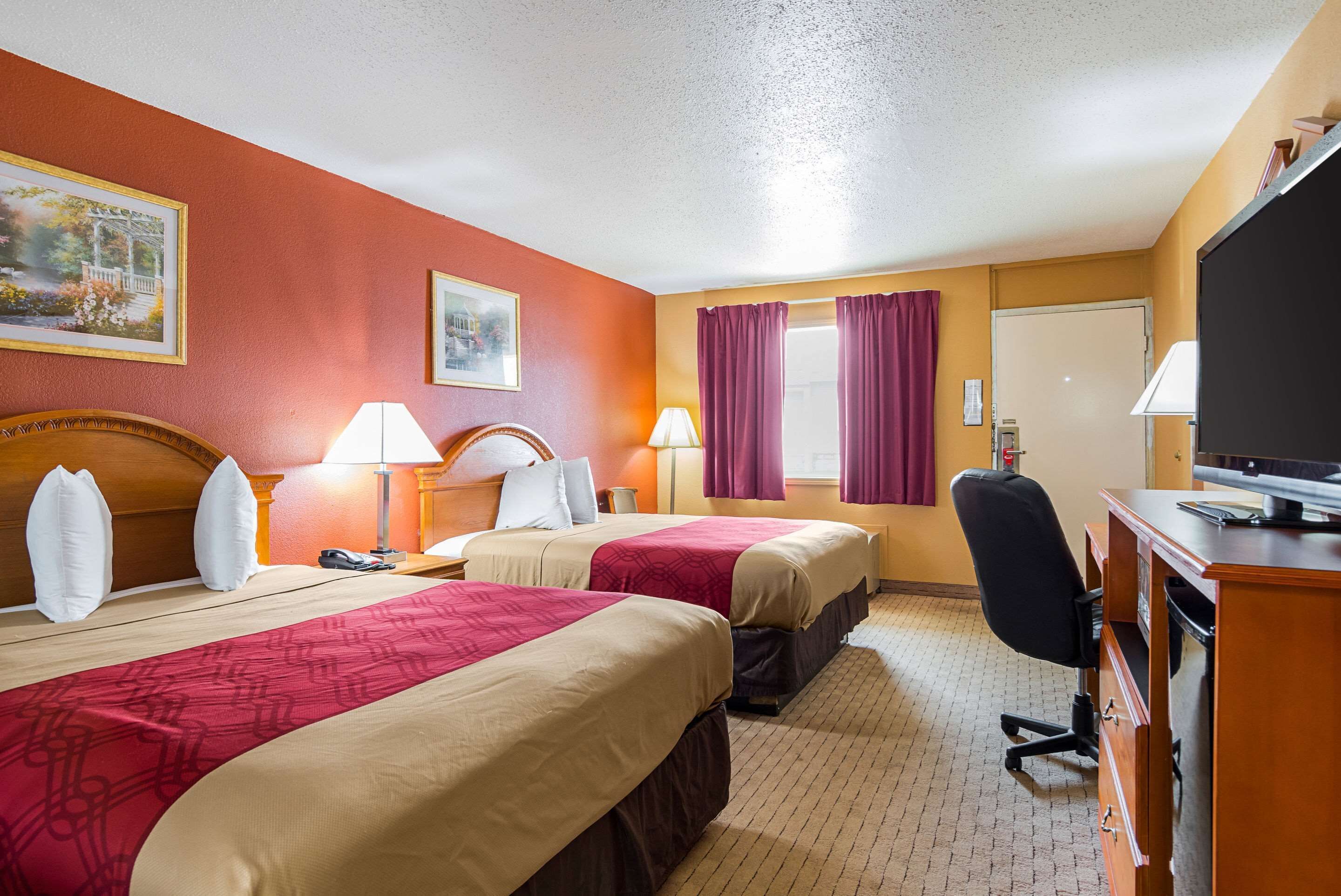 Ein Hotelzimmer mit zwei Betten, einem Schreibtisch, einem Sessel und einem Fernseher.