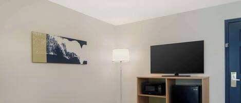 A hotel room with a flat-screen TV, a small table, a sofa, a lamp, and a microwave.