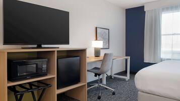 A hotel room with a flat-screen TV, a microwave, a desk with a chair, a lamp, and a bed.