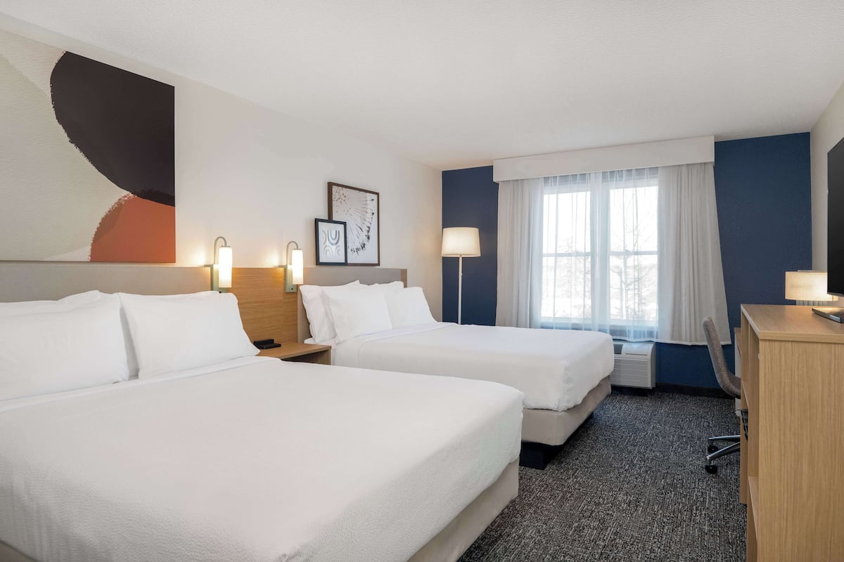 Een hotelkamer met twee bedden, een bureau, een stoel, een lamp en een raam met gordijnen.