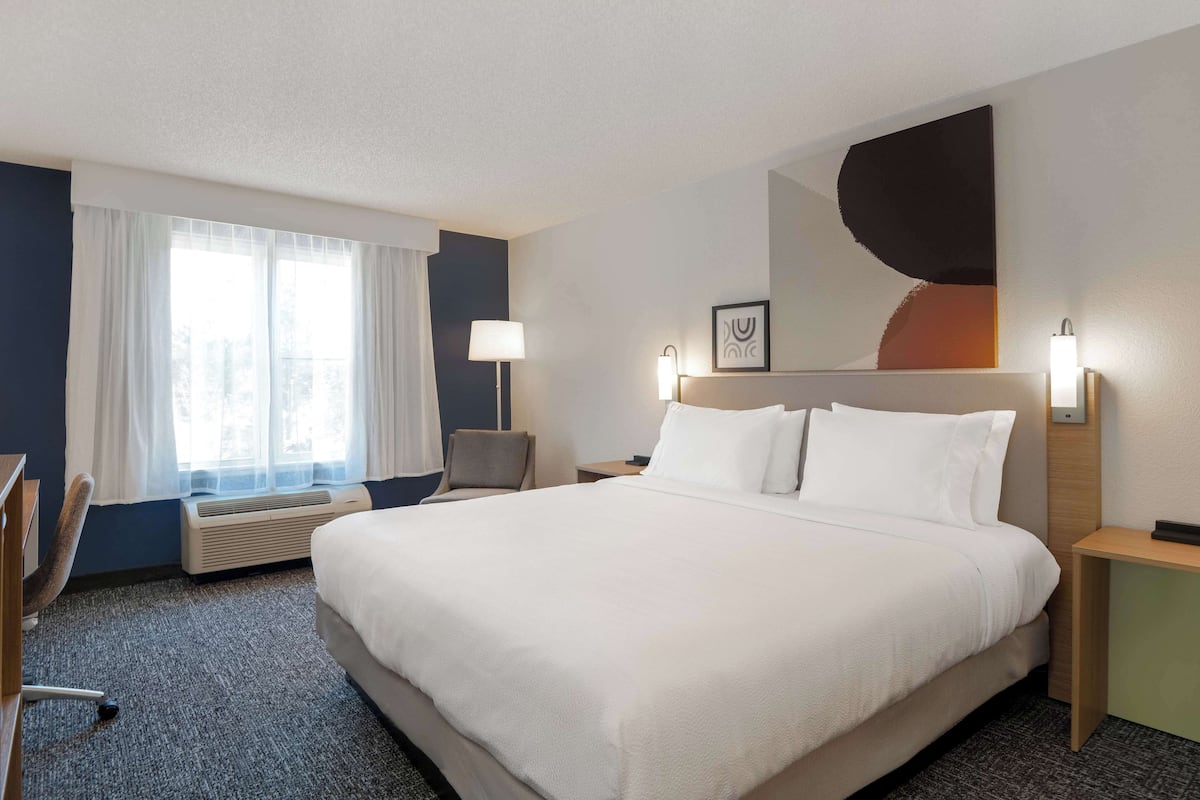 Hotelkamer met een groot bed, een bureau, een stoel, een raam met gordijnen, een wandlamp en een ingelijst schilderij.