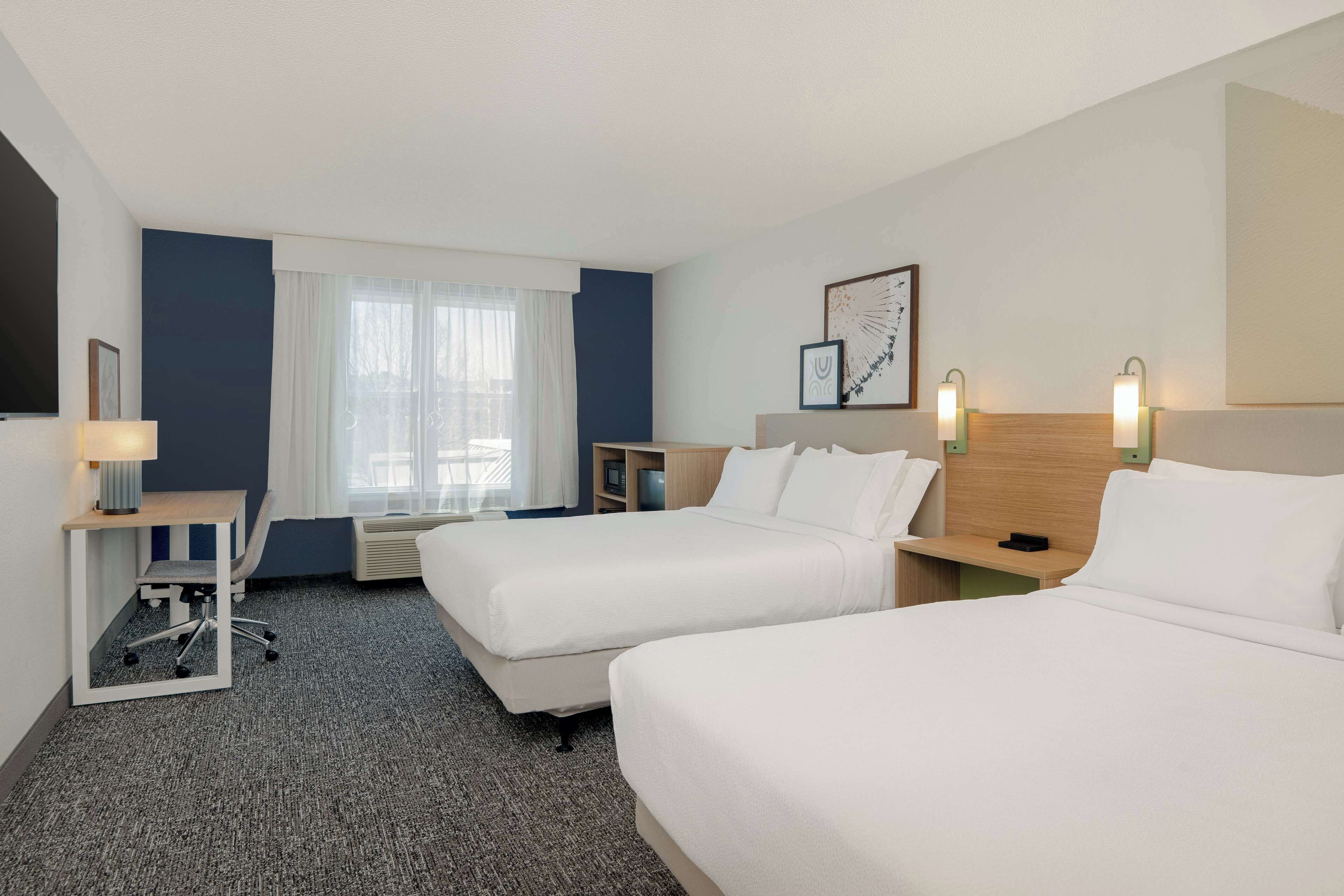 Une chambre d’hôtel avec deux lits, un bureau, une chaise, une télévision et une fenêtre avec des rideaux.