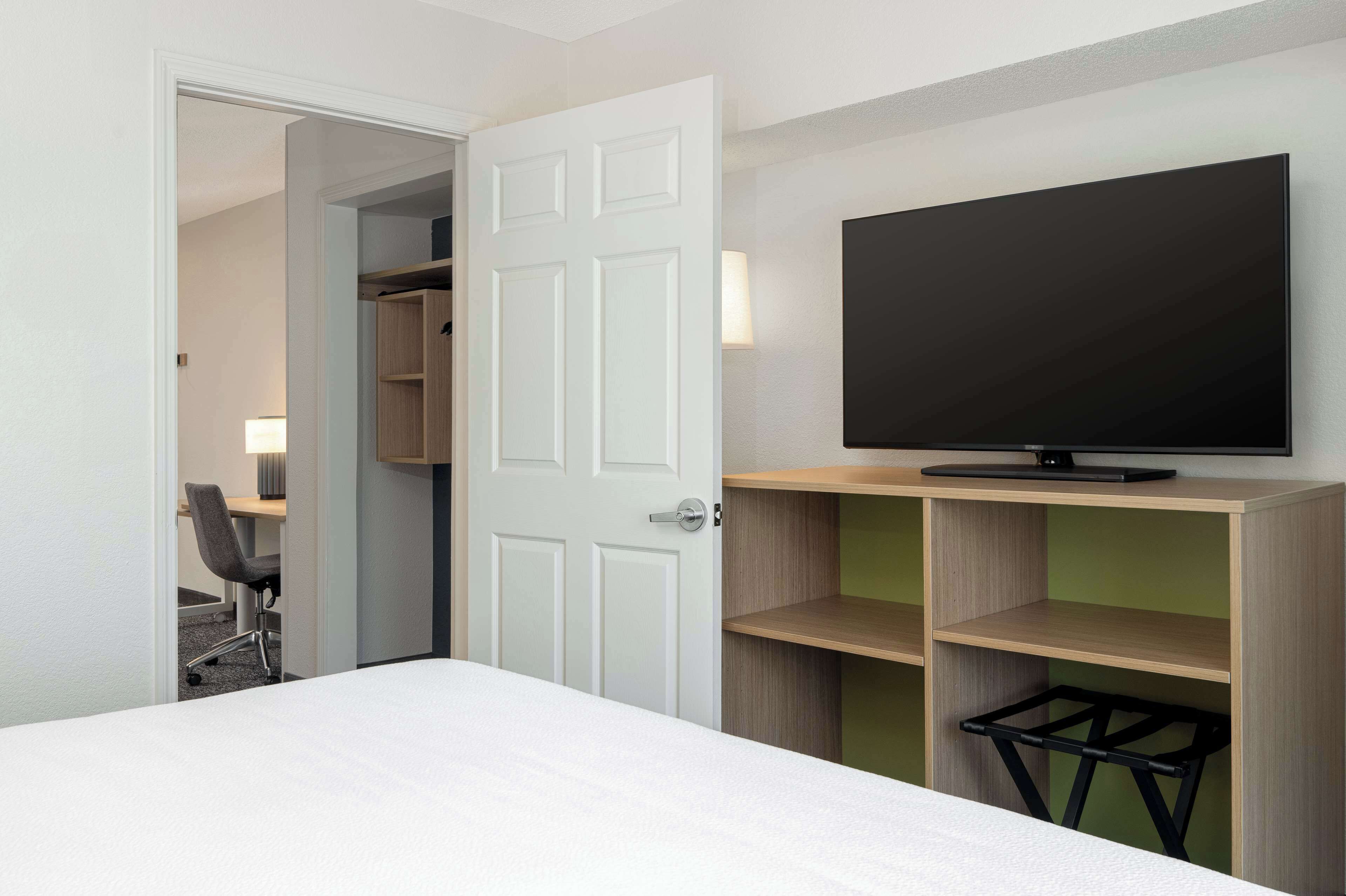 A hotel room with a bed, a TV on a stand, a desk with a chair, and a wardrobe.