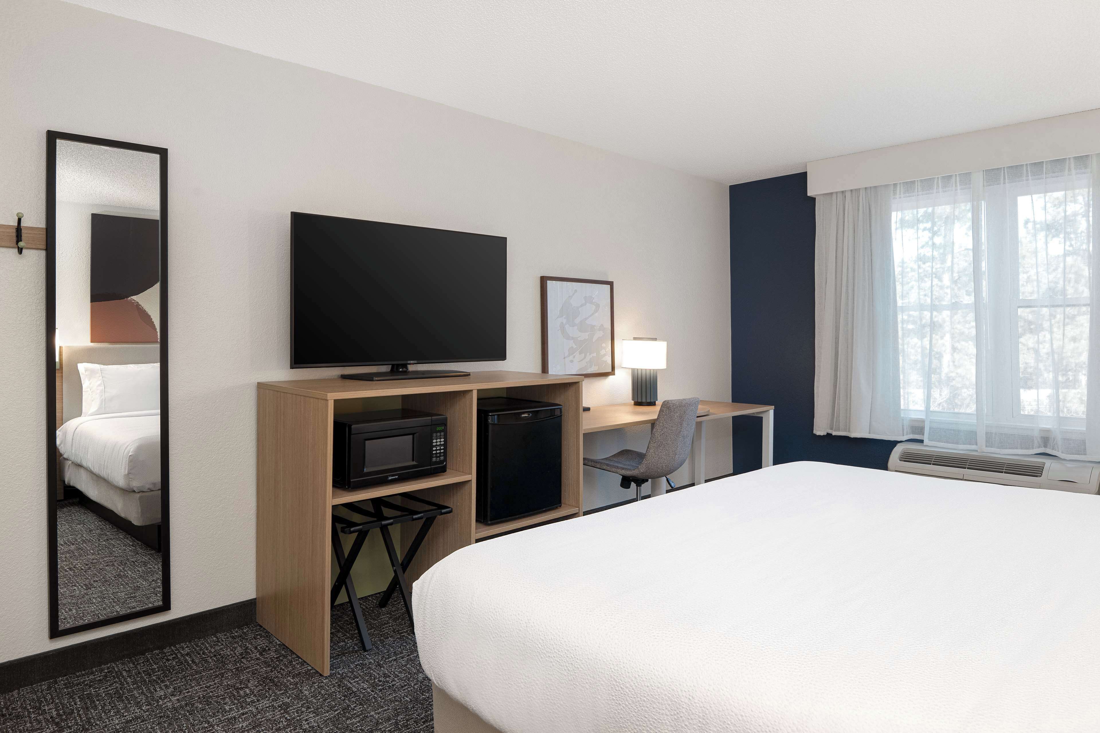 Ein Hotelzimmer mit einem großen Bett, einem Schreibtisch mit Computer, einem Fernseher, einer Mikrowelle und einem kleinen Kühlschrank.