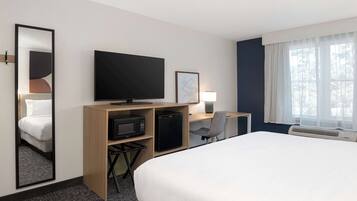 Ein Hotelzimmer mit einem großen Bett, einem Schreibtisch mit Computer, einem Fernseher, einer Mikrowelle und einem kleinen Kühlschrank.