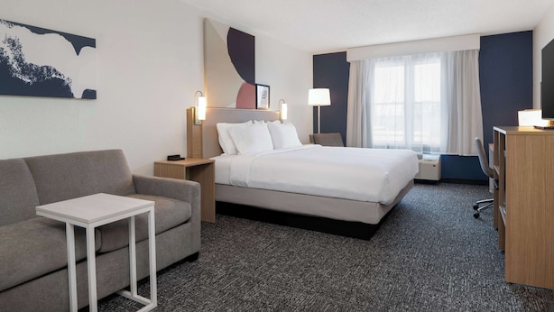 Una habitación de hotel con cama, sofá, mesita, escritorio y lámpara.