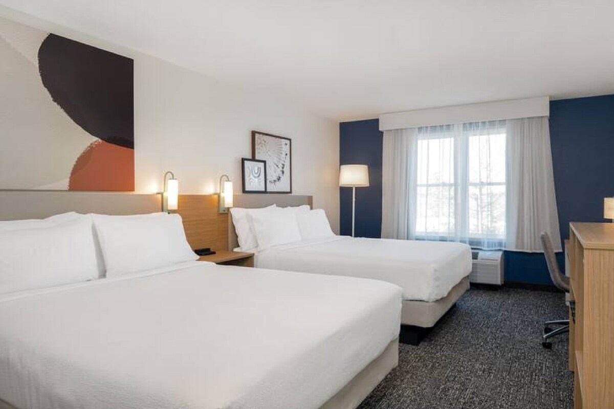 A hotel room with two beds, a desk, and a window with curtains.