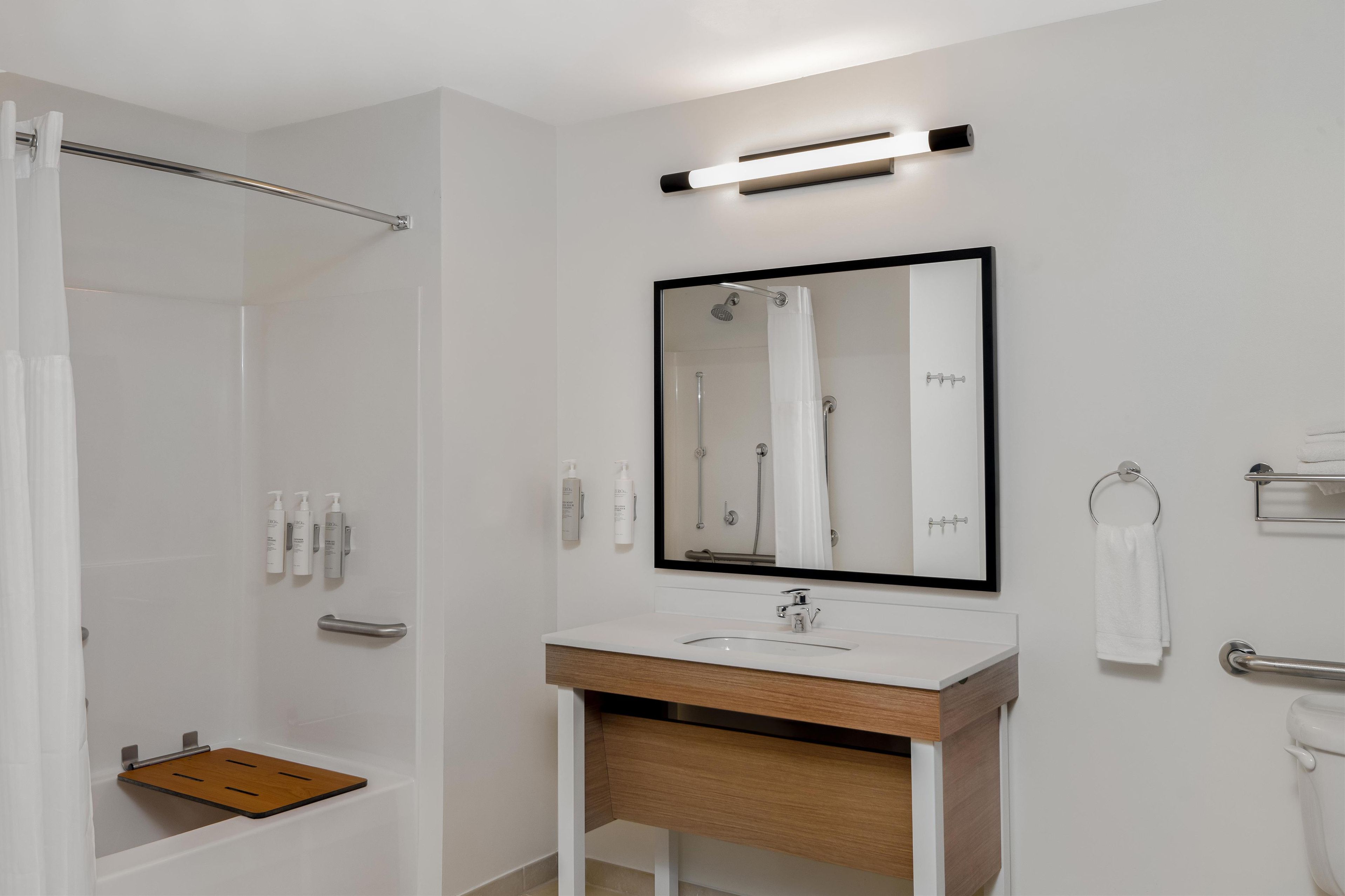 A modern bathroom with a shower, a sink with a wooden vanity, a mirror, and a towel rack.