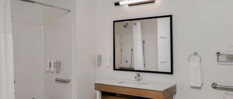 Un baño moderno con ducha, lavabo con tocador de madera, espejo y toallero.