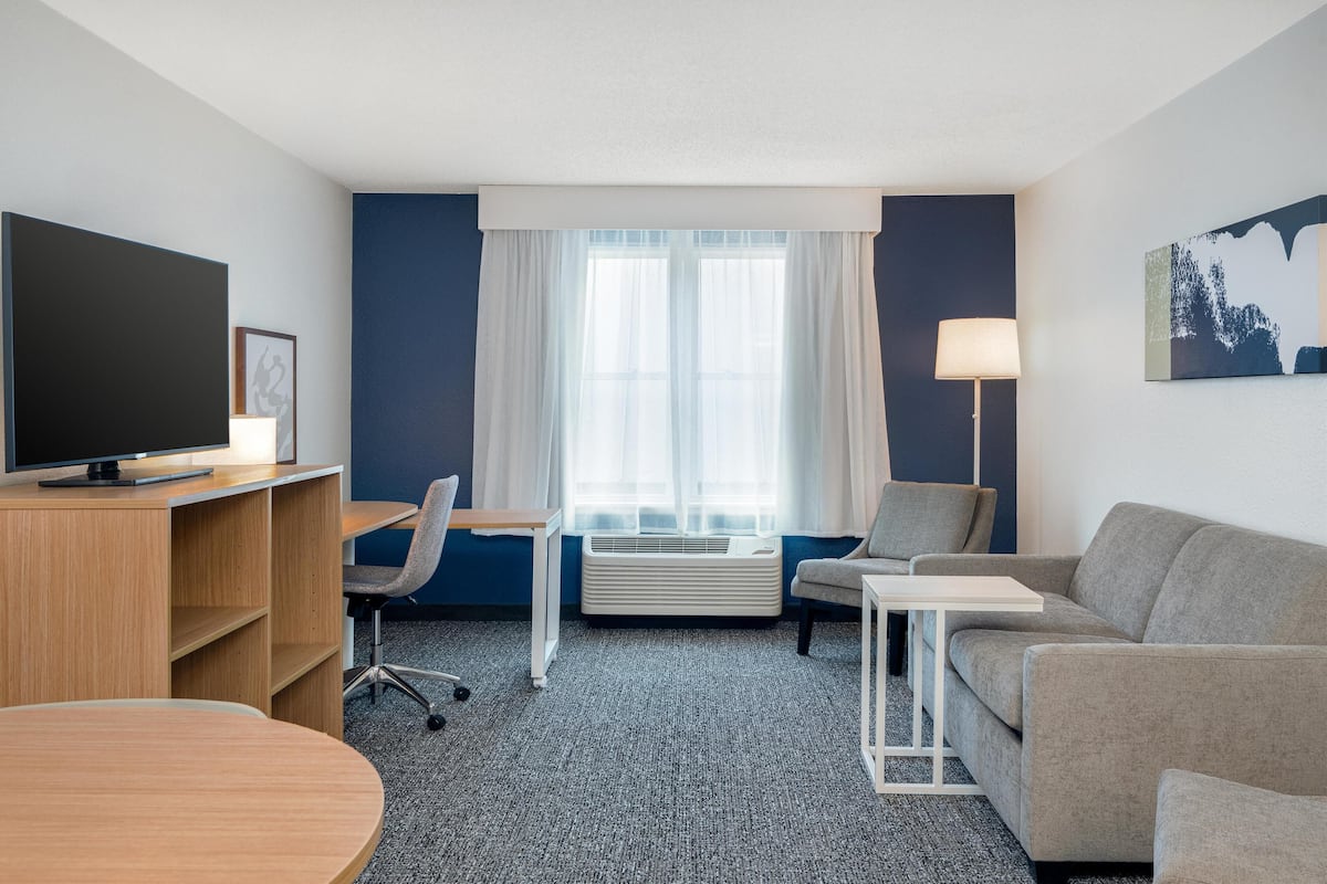 Een hotelkamer met een bureau, stoel, bank, televisie en airconditioning.