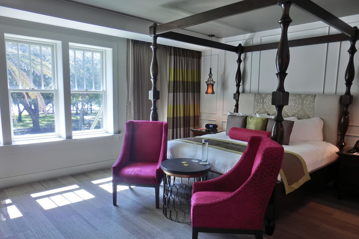Een hemelbed met hoofdbord, twee fauteuils, een klein rond tafeltje en een nachtkastje met lamp.