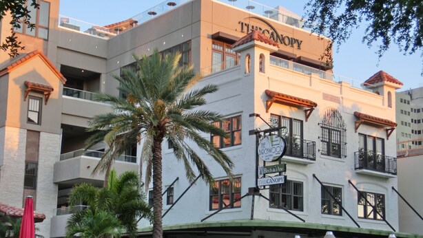 Un hotel de varios pisos con balcones, zona de estar exterior y una palmera.