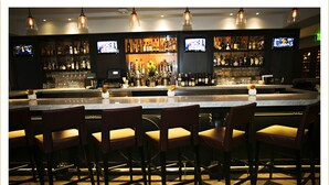 Un bar con varias televisiones, una amplia variedad de botellas de licor y taburetes.
