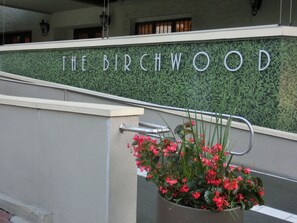 Une entrée d’immeuble avec une enseigne indiquant « THE BIRCHWOOD » et une main courante en métal.