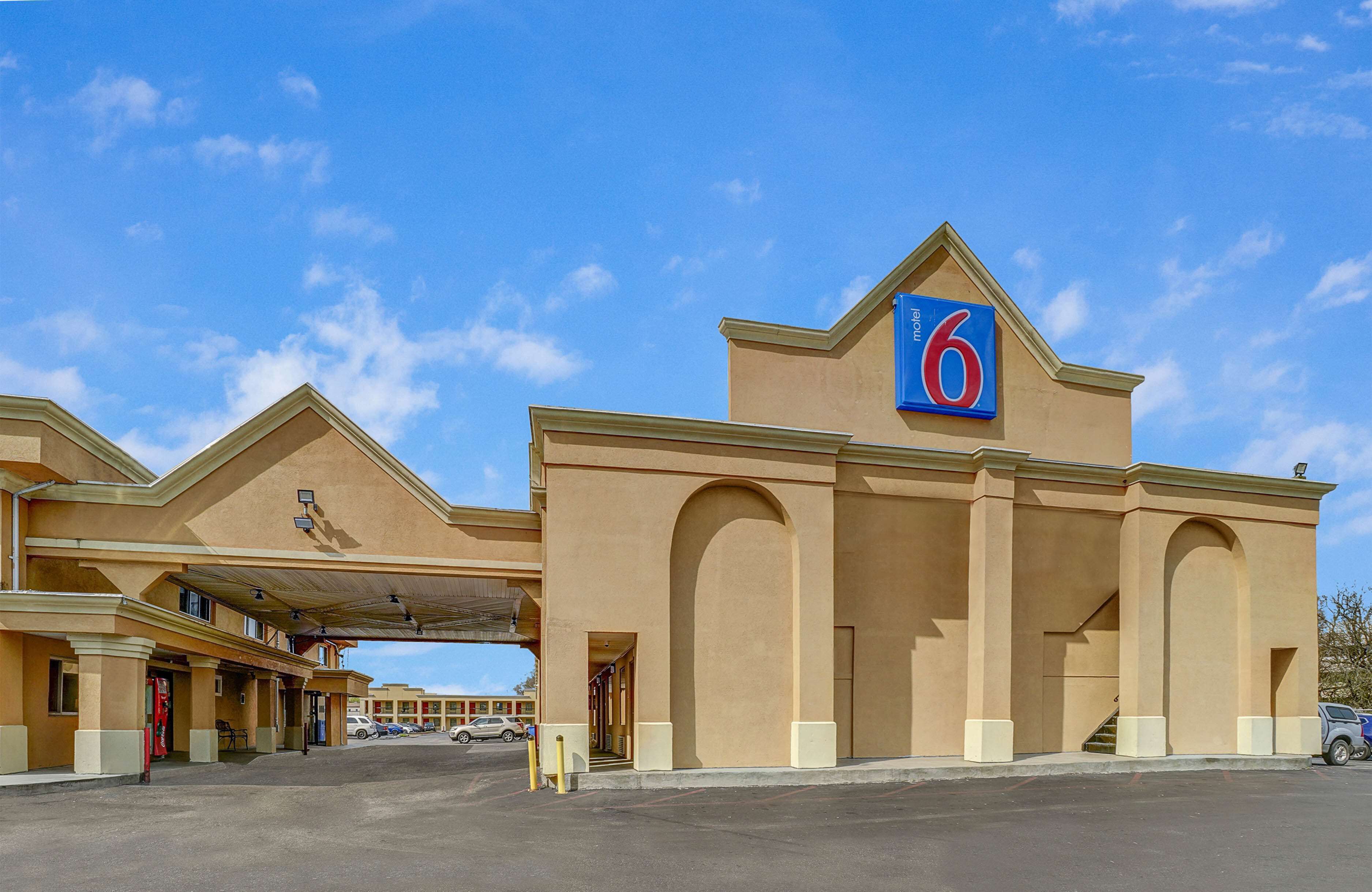 A 6-story hotel with a prominent '6' sign, multiple entry points, and a parking lot.