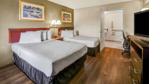 Ein Hotelzimmer mit zwei Betten, einem Schreibtisch mit Stuhl, einem Fernseher und zwei gerahmten Bildern an der Wand.