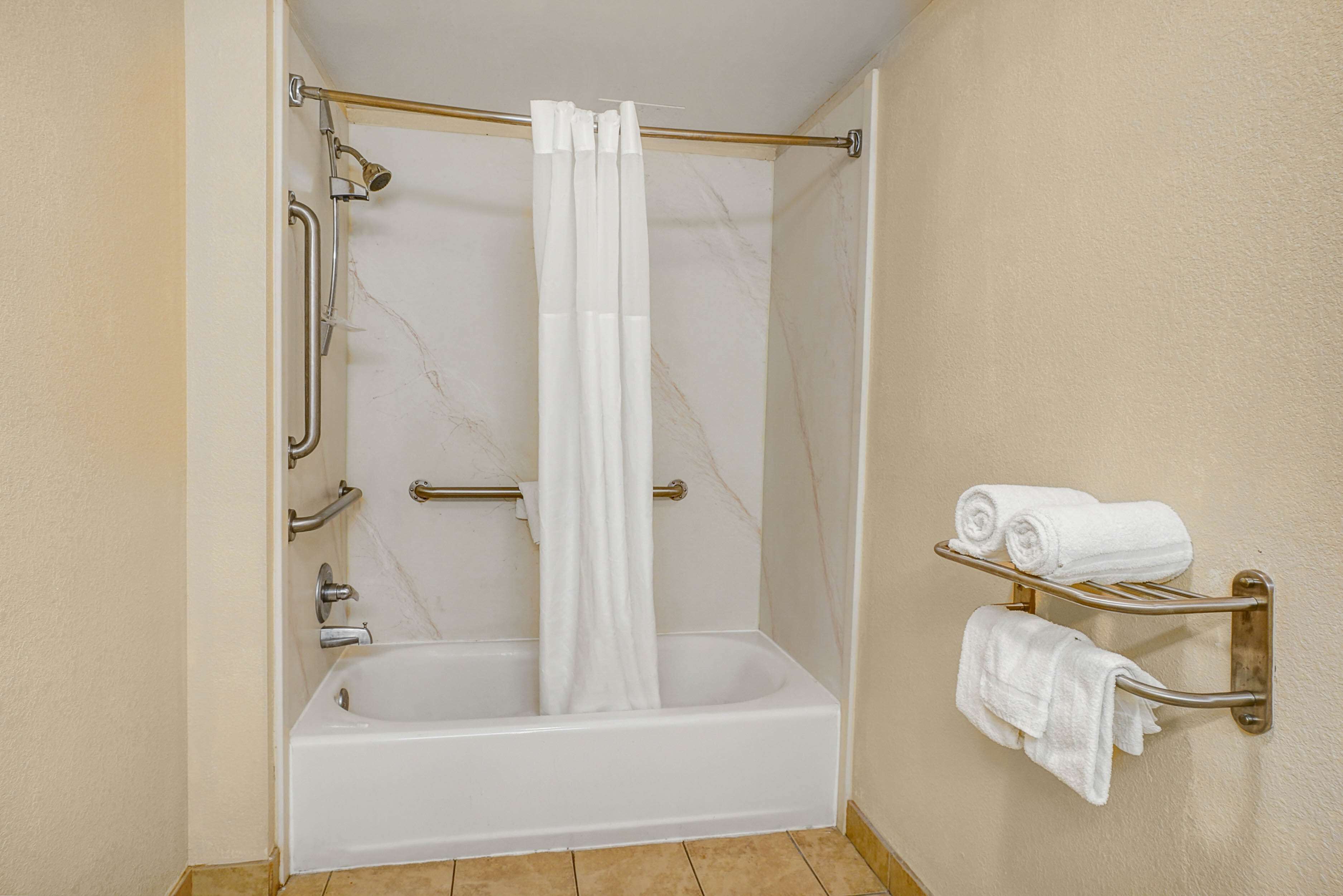A bathroom with a bathtub, a shower curtain, a towel rack with towels, and a handrail.