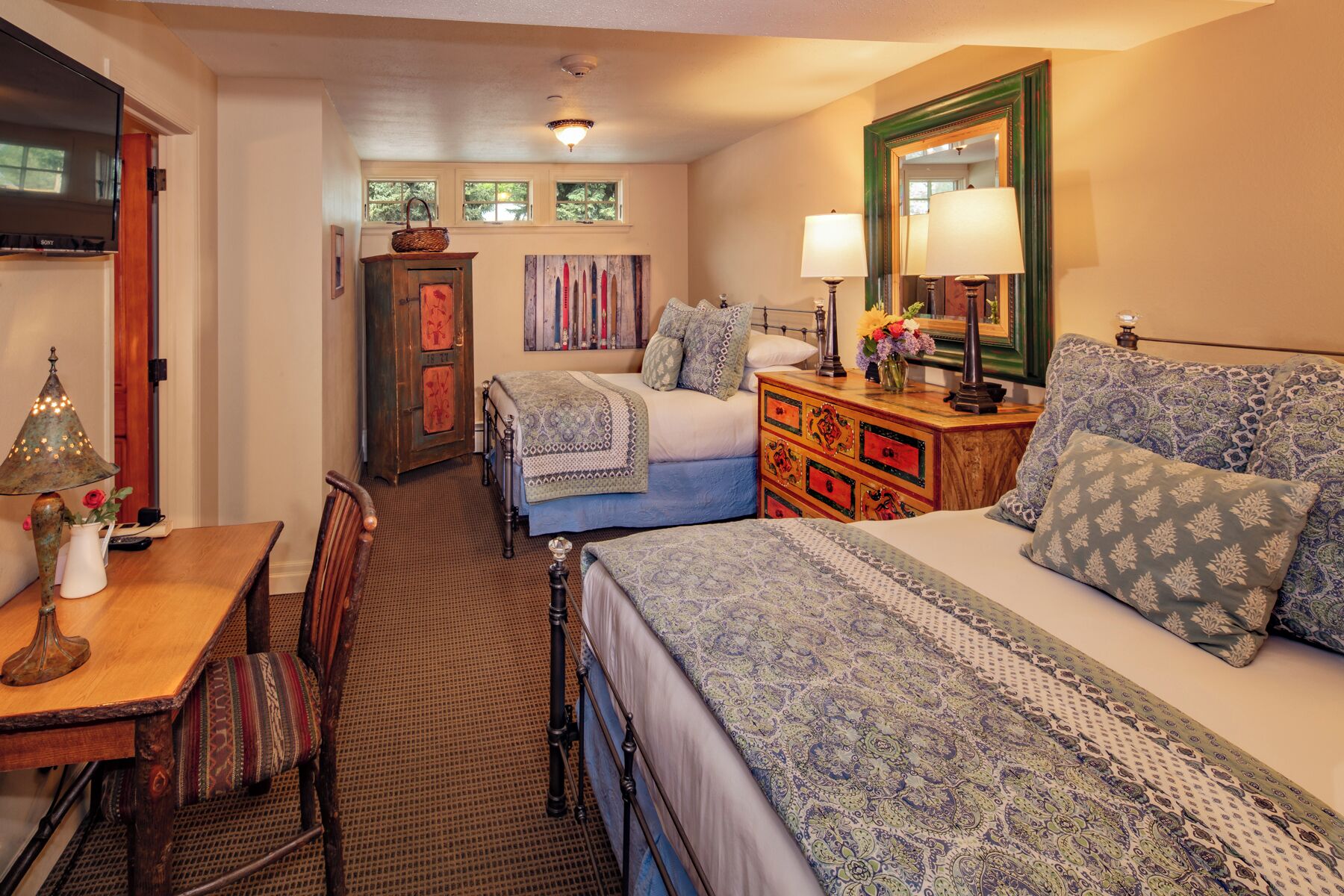 A bedroom with two beds, a dresser, a lamp, a TV, and a bookshelf.
