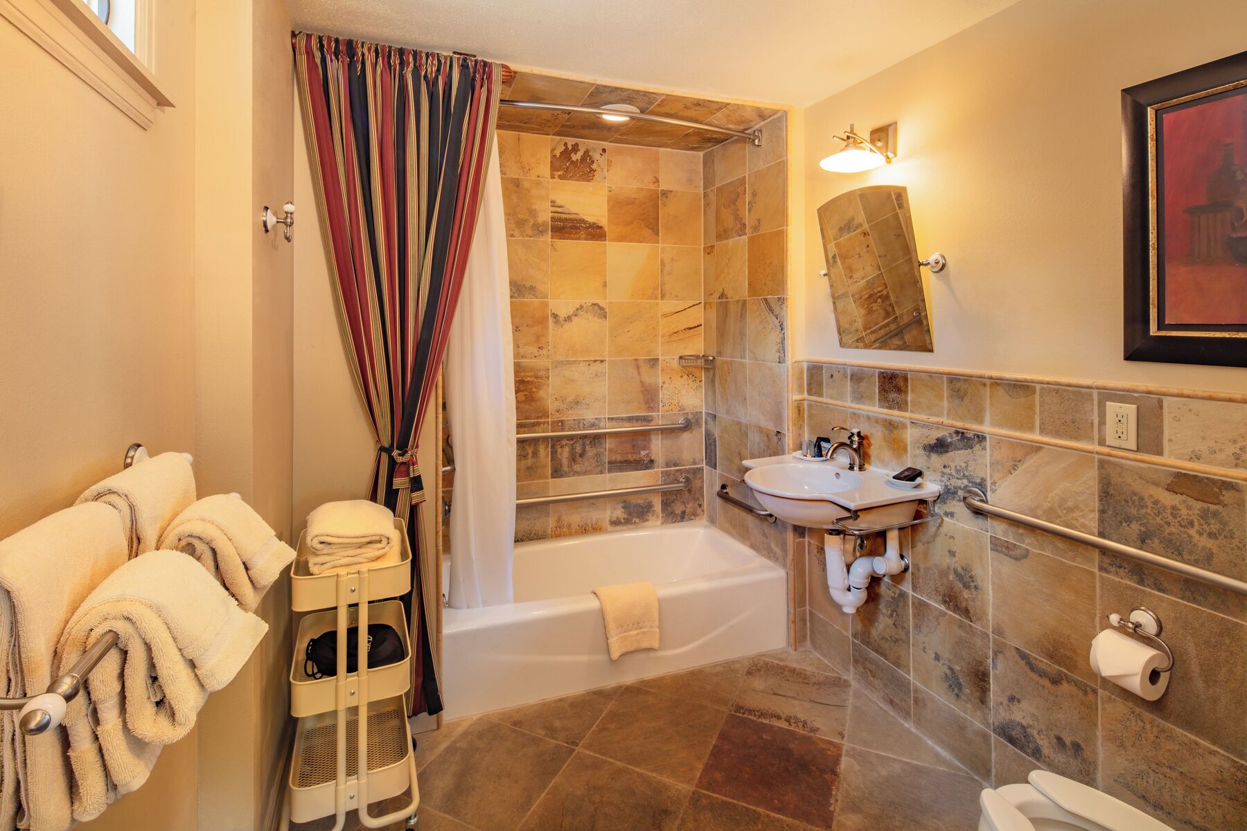 A bathroom with a bathtub, shower, and sink, featuring a tiled shower wall and a towel rack with towels.