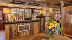 A wooden reception desk with framed artwork, a laptop, and a vase of flowers. - Annabelle Inn (Aspen)