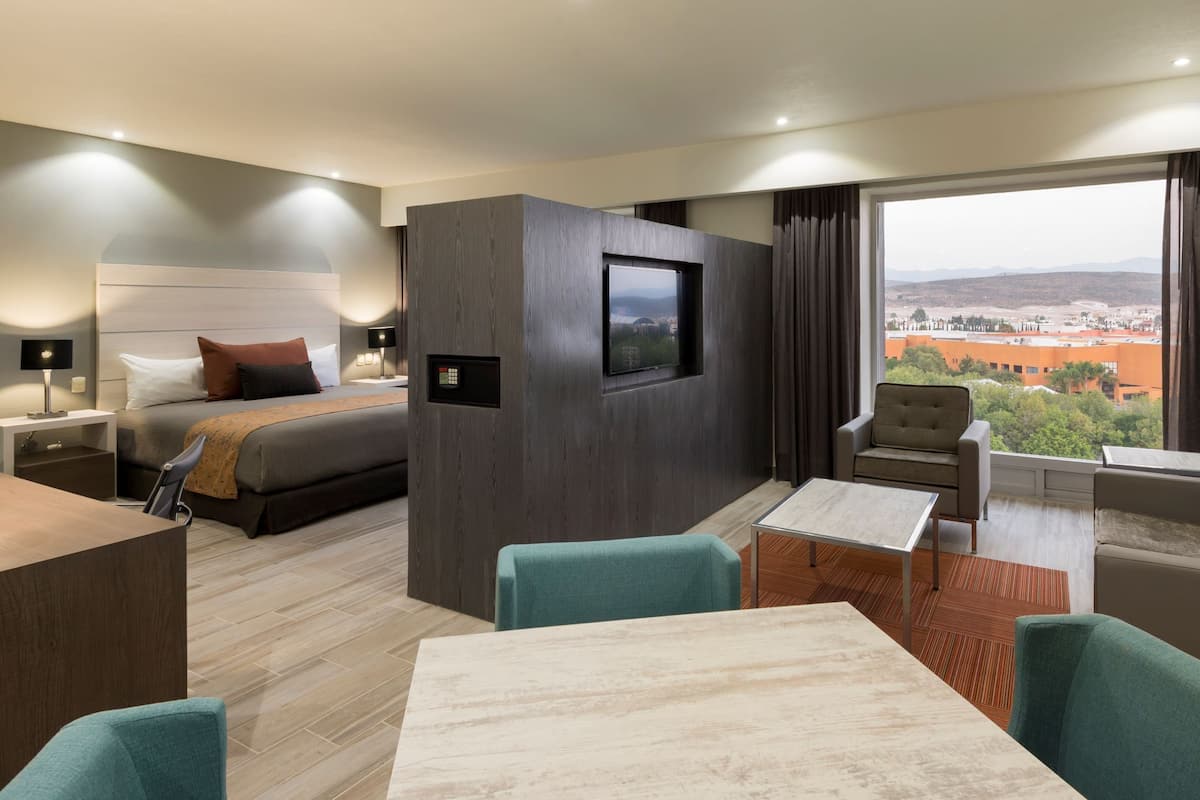 A hotel room with a bed, a desk, a chair, a table, and a view of the city.