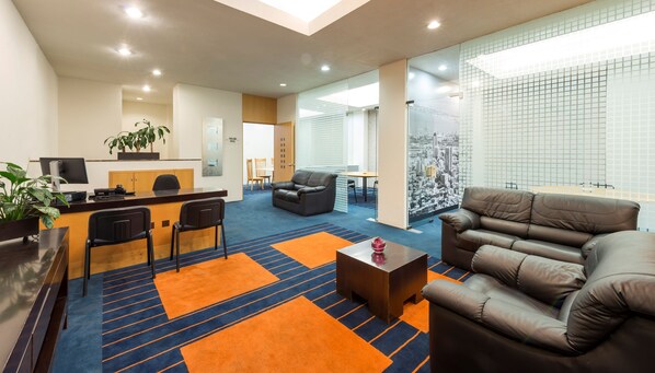 Un moderno vestíbulo de hotel con mostrador de recepción, zona de estar y un amplio ventanal con vistas a la ciudad.