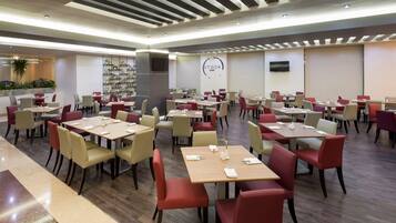 Um restaurante moderno com várias mesas e cadeiras, um quadro de menu visível e uma televisão na parede.