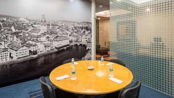A conference room with a round table, four chairs, and a large cityscape mural on the wall.