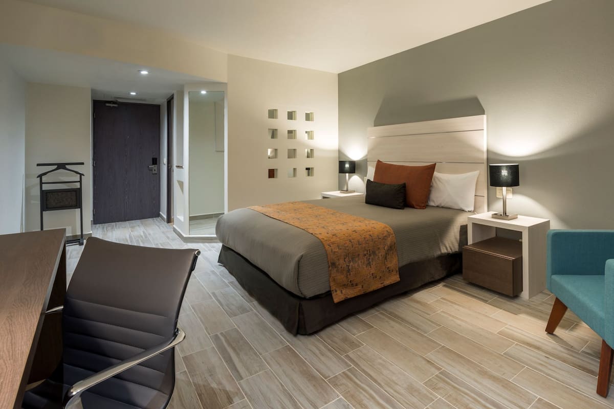 A modern hotel room with a bed, bedside tables, a chair, and a desk.
