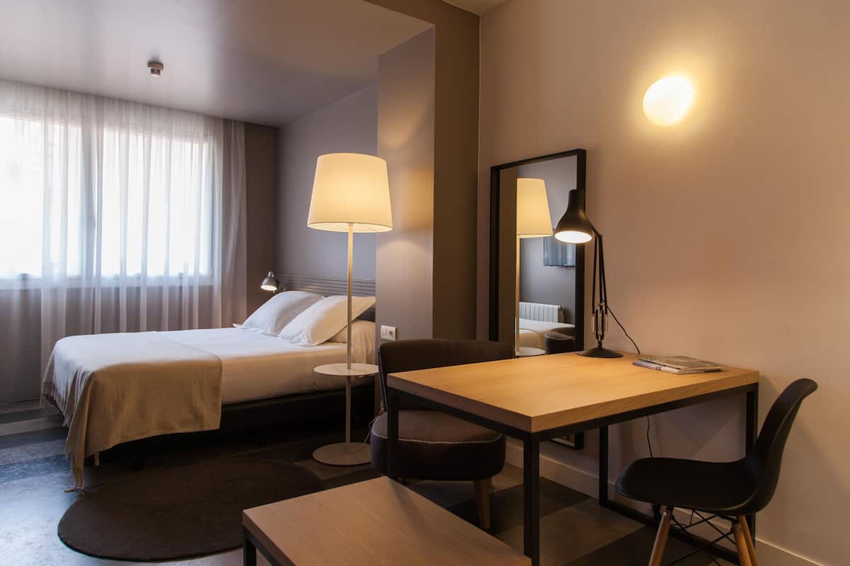 Habitación de hotel con cama, escritorio, silla, lámpara y espejo.