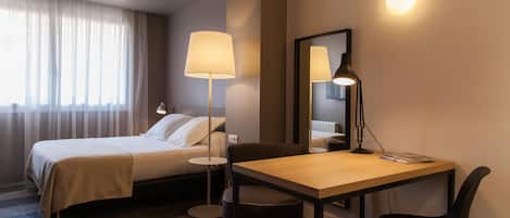 Habitación de hotel con cama, escritorio, silla, lámpara y espejo.