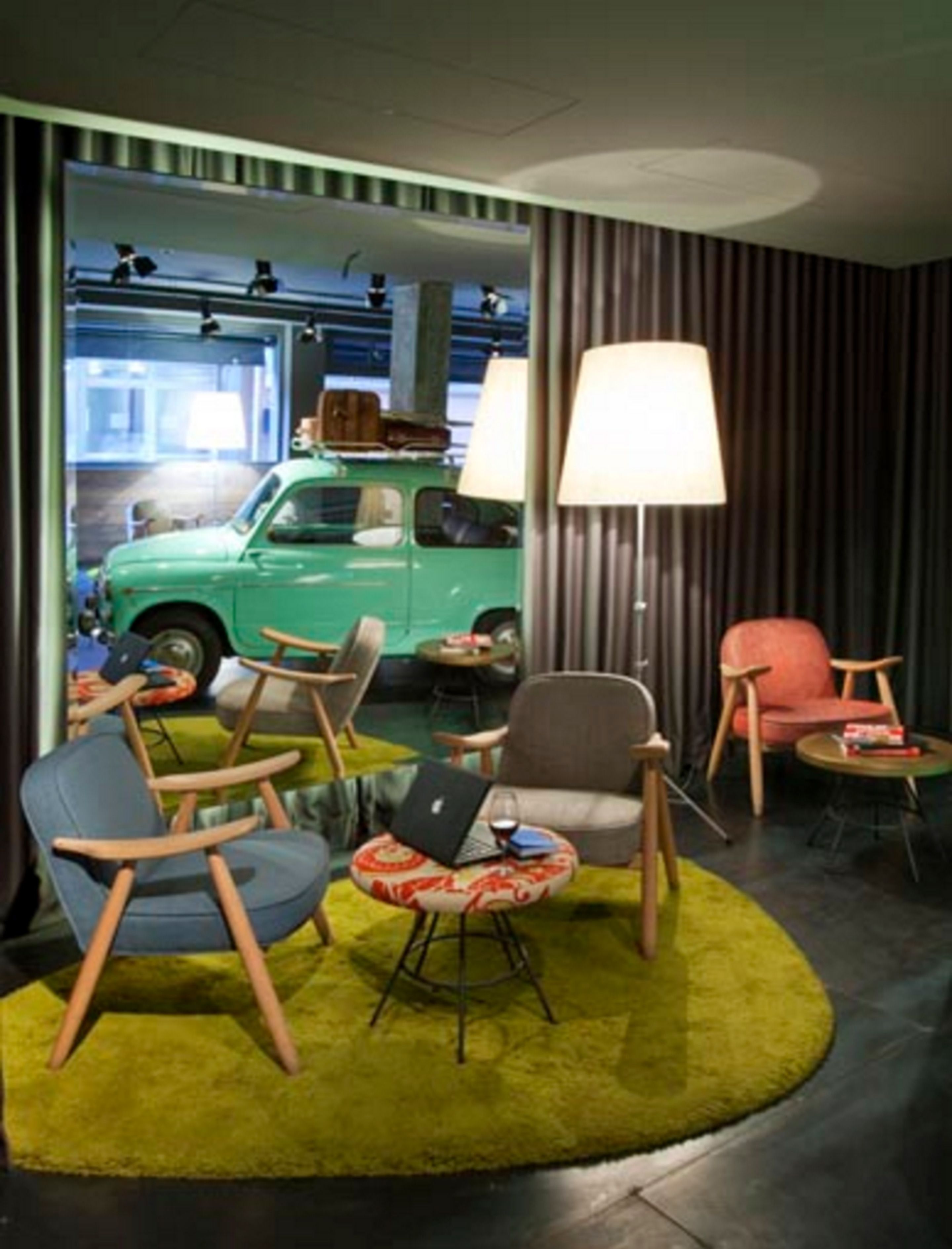 A modern interior with a green vintage car in the background, a round coffee table, and two armchairs.